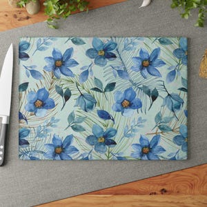 May include: A blue and green floral pattern on a glass cutting board. The flowers are watercolor style and have a light blue background.