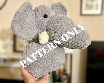 May include: A gray crocheted elephant plush toy with a white crocheted tusk. The toy is being held by a hand. The text "PATTERN ONLY" is superimposed on the image.