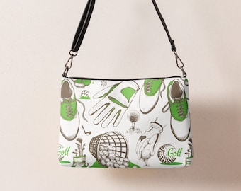 May include: A white crossbody bag with a black strap. The bag has a green and brown print of golf-themed illustrations, including golf shoes, golf balls, golf clubs, and golf gloves. The text "Golf" appears twice on the bag.