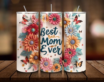 Könnte beinhalten: Ein zylindrischer Becher mit Strohhalm auf cremefarbenem Hintergrund, verziert mit blumenartigen Papierillustrationen in Rosa, Orange und Blau, Schmetterlingen sowie dem dunkelblauen Schriftzug "Best Best Mom Ever" auf der Vorderseite.