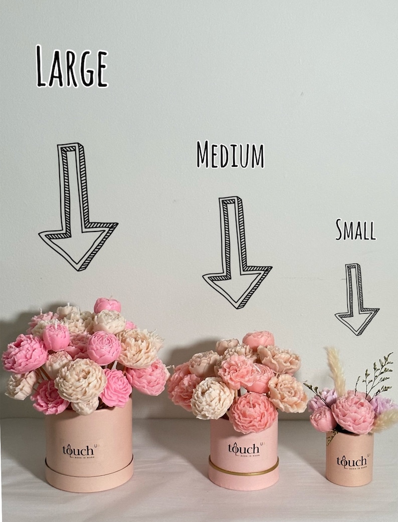 Pode incluir: Tr&ecirc;s arranjos florais em caixas redondas rosa com as etiquetas "Large", "Medium" e "Small". Os arranjos apresentam flores rosa e creme. As caixas t&ecirc;m uma faixa dourada e a palavra "touch" impressa.