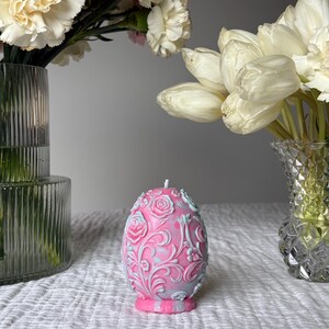 May include: A pink and blue floral patterned candle shaped like an egg. The candle is sitting on a white surface.