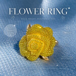 May include: A statement flower ring with a bold design. The ring features a large, yellow, crystal-covered flower with gold accents. The text "FLOWER RING" and "STATEMENT JEWELRY" are visible. The ring is perfect for any occasion.