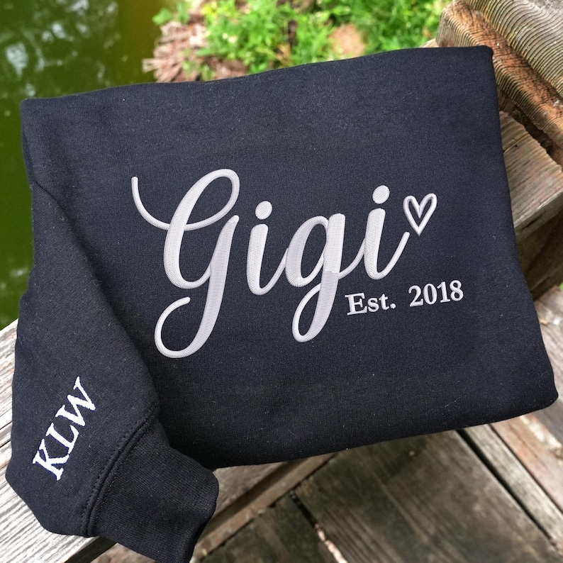 Black embroidered sweatshirt featuring "Gigi EST. 2018" with a heart. Personalized grandma sweatshirt gift for Mother’s Day, Christmas, or birthdays. Cozy vintage-washed fabric perfect for proud grandmothers celebrating their family legacy.