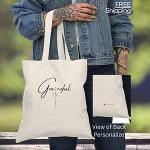 May include: A cream-coloured tote bag featuring the word "Graceful" in a cursive font. Beneath it is the phrase "walking in Hope". The back of the bag is shown with a small red heart and the text "your name".