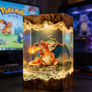 May include: A rectangular lamp featuring a resin-encased Charizard figure sitting on a rocky base. The orange dragon-like creature has blue wings and emits a flame from its mouth. The lamp is framed by natural wood at the top and bottom.