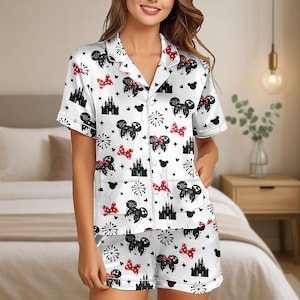 Könnte beinhalten: Weißes Satin-Pyjama-Set mit einem Muster aus schwarzen Mickey Mouse-Silhouetten, roten Tupfen-Schleifen und schwarzen Schloss-Illustrationen. Das kurzärmelige Oberteil hat einen Reverskragen und Taschen. Die Shorts haben einen elastischen Bund.