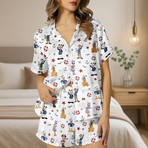 Puede incluir: Conjunto de pijama blanco con estampado de temática náutica con personajes de dibujos animados, incluyendo Mickey Mouse, Donald Duck y Pluto. El conjunto incluye una camisa con botones de manga corta y pantalones cortos.