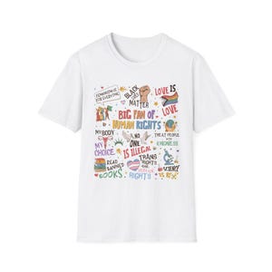 Puede incluir: Camiseta blanca con un diseño gráfico colorido. El diseño incluye frases como "Black Lives Matter", "Human Rights" y "Love is Love". Otros textos incluyen "Feminism is for Everyone" y "Trans Rights are Human Rights."