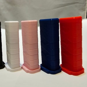 Könnte beinhalten: Fünf 3D-gedruckte Griffe in verschiedenen Farben: Schwarz, Weiß, Rosa, Blau und Rot. Jeder Griff hat eine strukturierte Oberfläche und eine abgerundete Basis.
