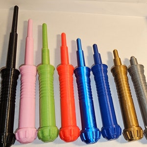 May include: Nine 3D printed lightsaber hilts in various colors, including black, pink, green, red, blue, gold, and gray. The hilts have a textured, ribbed design and a rounded tip.