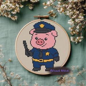 May include: Cross-stitch embroidery of a pig wearing a police uniform, including a blue hat and jacket with a gold badge and belt. The pig is holding a black object. The text "Bleach Stitch" is at the bottom.