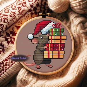 Peut inclure: Une broderie au point de croix dans un cercle en bois représente un rat brun portant un bonnet de Père Noël et portant des cadeaux emballés. La broderie est posée sur un fond texturé et chaleureux avec le texte "Bleach Stitch".