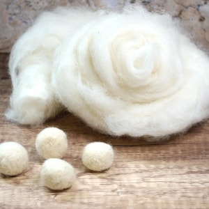 May include: A pile of white wool roving with four small white wool balls on a wooden surface.