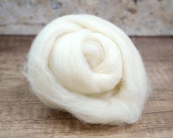 May include: A close-up of a ball of soft, white wool roving. The wool is tightly coiled, showing a spiral pattern. The background is a light brown wooden surface.