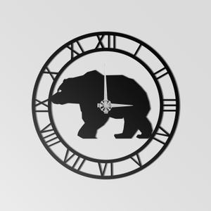 Op de afbeelding: Zwarte metalen wandklok met een berensilhouet in een Romeinse cijferwijzerplaat. De wijzers zijn zilverkleurig. De beer is gecentreerd. Het ontwerp van de klok is modern en minimalistisch, geschikt voor woondecoratie.