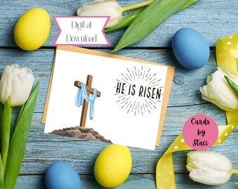 May include: A digital download Easter card with a white background featuring a wooden cross with a blue cloth draped over it. The text "He is Risen" is written in black with a sunburst design behind it. The card is surrounded by yellow and blue Easter eggs and white tulips.