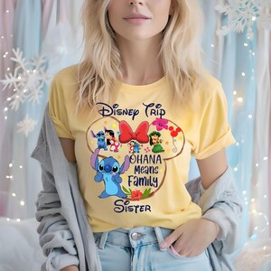 May include: Yellow t-shirt featuring a Disney Trip design with Stitch and other characters. The design includes the text "Ohana Means Family Sister" in a playful font. The shirt is a short-sleeved crew neck.