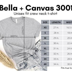 May include: A light gray Bella + Canvas 3001 unisex fit crew neck t-shirt. The image includes a size chart with measurements in inches for sizes XS to 4X. The shirt is paired with denim shorts and a sprig of dried grass.