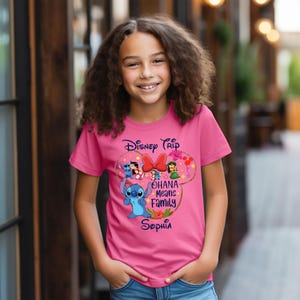 May include: A pink t-shirt featuring a Disney-themed design. The design includes the text "Disney Trip" and "Ohana Means Family" with a cartoon character. The name "Sophia" is also included. The shirt is short-sleeved.