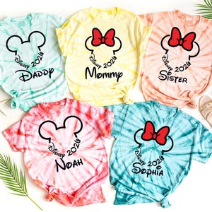 Pu&ograve; includere: Magliette tie-dye in tonalit&agrave; blu, giallo, rosa e pesca. Ogni maglietta presenta un design a forma di testa di Topolino o Minnie con la scritta "Disney 2020" e il nome di un familiare, come "Daddy" o "Mommy".