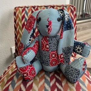 May include: A patchwork bunny toy made from blue and red bandana fabric. The bunny is sitting on a chair with a colorful patterned fabric.