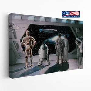 May include: A rectangular canvas print featuring a scene from Star Wars with C-3PO, R2-D2, and two figures looking out a large window at a space nebula and a ship. The print includes a small rectangular logo in the corner that reads MADE IN USA.