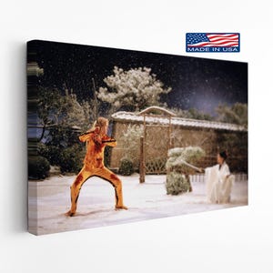 May include: A rectangular canvas print depicting a scene in the snow with a person in a yellow tracksuit holding a sword and another person in a white robe holding a sword. The image includes a small logo in the corner with the text MADE IN USA.