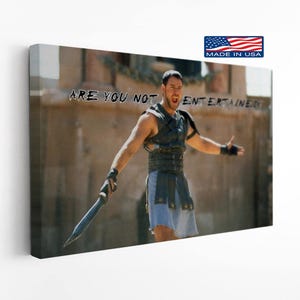 May include: A rectangular canvas print featuring a scene from the film Gladiator, showing a warrior in dark leather armor and a light blue tunic holding a sword with arms outstretched. The text ARE YOU NOT ENTERTAINED is printed in black.