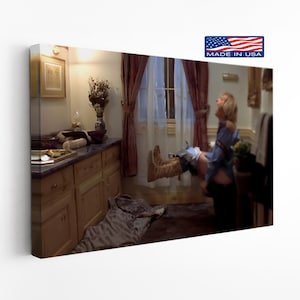 May include: A framed canvas print featuring a scene from a movie. The image shows a person in a bathroom, mid-air, with a look of surprise. The room has wooden cabinets, a window with curtains, and a rug on the floor. The print has a "Made in USA" logo.