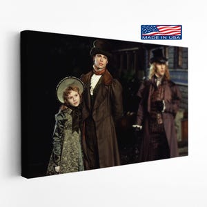May include: A canvas print featuring a scene from a movie. The image shows three people in period clothing. The man in the center wears a brown coat and top hat. The print has a "Made in USA" label.