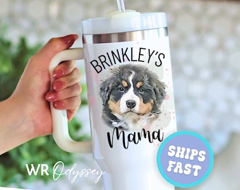 May include: White travel mug with a handle, featuring a portrait of a Bernese Mountain Dog puppy. The mug is labeled "Brinkley's Mama" in black script. A blue and purple circle with "SHIPS FAST" is also visible.