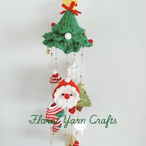 May include: A crocheted Christmas mobile with a green tree, Santa Claus, a stocking, a bell, and a star. The mobile is hanging from a white wall and has the text "Floral Yarn Crafts" on it.