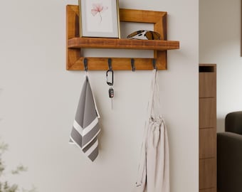 May include: A wooden wall-mounted shelf with a picture frame, sunglasses, and hooks. A gray and white striped towel, a key, and a drawstring bag hang from the hooks. The shelf is mounted on a light-colored wall.