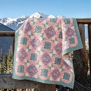 May include: A quilt featuring a geometric pattern of squares and diamonds in shades of soft pink, sage green, and lavender. The fabric displays a floral print throughout, with intricate stitching visible across the surface of the textile.
