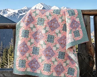 May include: A quilt featuring a geometric pattern of squares and diamonds in shades of soft pink, sage green, and lavender. The fabric displays a floral print throughout, with intricate stitching visible across the surface of the textile.