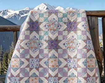 May include: A quilted blanket featuring a geometric star pattern in shades of lavender, light blue, and cream. The fabric squares display intricate floral and animal motifs, with visible stitching throughout the textile surface.
