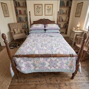 May include: A wooden four-poster bed frame with a carved headboard, dressed in a quilt featuring a patchwork star pattern in shades of lavender, light blue, and white. Two matching lavender pillowcases with floral embroidery sit at the head.