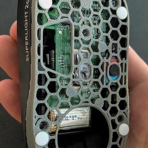 May include: A black and grey computer mouse with a honeycomb pattern on the underside. The mouse is labelled "SUPERLIGHT 2c". Internal components, including a circuit board, are visible through the open design.