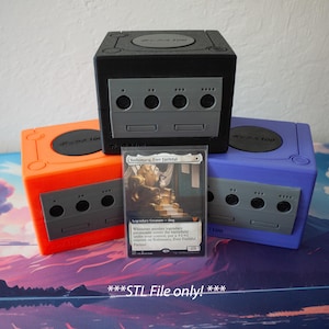 Op de afbeelding: Drie 3D-geprinte GameCube-controllers in oranje, zwart en blauw. De controllers zijn op elkaar gestapeld. Voor de controllers ligt een Magic: The Gathering-kaart. De kaart heeft de titel "Soulherder, the Faithful".