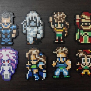 May include: Eight pixel art figures, likely from a video game, arranged on a dark surface. The figures are made of colorful plastic beads, depicting various characters with distinct outfits and features. The figures vary in size and color.