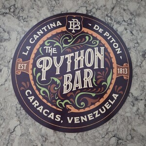 Op de afbeelding: Een rond bord met een donkerpaarse achtergrond en decoratieve lichtgroene en bruine krullen. De tekst luidt The Python Bar, La Cantina De Piton, Caracas, Venezuela, Est 1813, inclusief een kleine slangenillustratie en een logo.