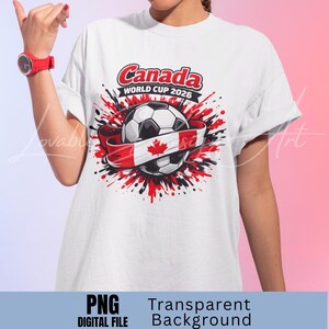 Puede incluir: Camiseta blanca con un dise&ntilde;o de bal&oacute;n de f&uacute;tbol envuelto en una bandera canadiense. El texto "Canada WORLD CUP 2026" est&aacute; en rojo y negro. El dise&ntilde;o incluye salpicaduras de pintura rojas y negras.