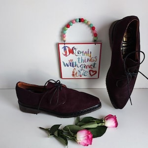 Może przedstawiać: Dwie pary bordowych skórzanych butów sznurowanych z czarnymi sznurówkami. Buty mają spiczasty nosek i grubą podeszwę. Buty leżą na białym tle z tabliczką z napisem "Do small things with great love".