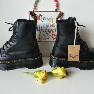 May include: A pair of black leather platform boots with yellow stitching and a Dr. Martens tag. The boots have a lace-up design and a thick platform sole.