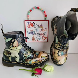 Peut inclure: Une paire de bottes en cuir noir avec un imprimé graphique coloré. Les bottes ont des lacets et une semelle épaisse. Les bottes sont posées sur une surface blanche avec une pancarte qui dit "Faites de petites choses avec beaucoup d'amour".