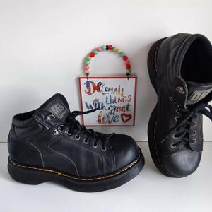 Könnte beinhalten: Zwei Paar schwarze Lederstiefel mit Schnürsenkeln. Die Stiefel haben dicke Sohlen und sind abgenutzt. Die Stiefel befinden sich auf einem weißen Hintergrund.