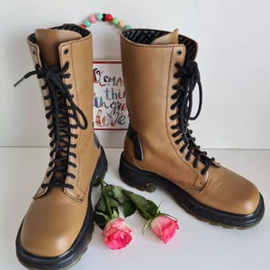 Può includere: Un paio di stivali marroni in pelle con lacci e suole nere. Gli stivali hanno un tacco spesso e sono realizzati in pelle morbida e flessibile.