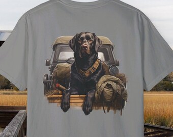 May include: A gray t-shirt with a black Labrador Retriever sitting in the back of a jeep. The dog is wearing a brown collar and looking back at the camera. The jeep is filled with camping gear.