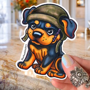 May include: A sticker featuring a cartoon Rottweiler puppy wearing a green military-style hat. The puppy has black and orange fur, with a purple crayon in its mouth. The sticker has the text "SharkKasmStickers" on the side.